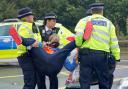 Police officers detain a protester from Insulate Britain occupying a roundabout leading from the M25 motorway to Heathrow Airport in London (photo: PA)