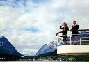 A stylish couple cruise along a fjord past the tiny port of Lyngseidet, Norway. Around 1965. Waterline Collection