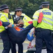 Police officers detain a protester from Insulate Britain occupying a roundabout leading from the M25 motorway to Heathrow Airport in London (photo: PA)