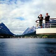 A stylish couple cruise along a fjord past the tiny port of Lyngseidet, Norway. Around 1965. Waterline Collection